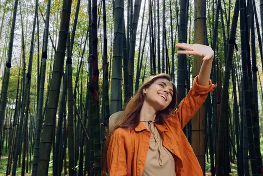 Улыбающаяся девушка в оранжевой куртке любуется бамбуковым лесом