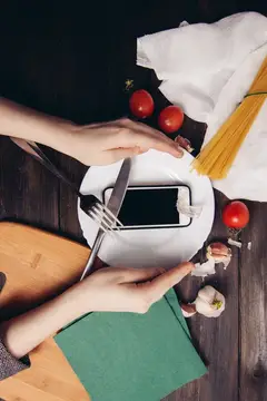 Руки держат смартфон над тарелкой с приборами среди продуктов