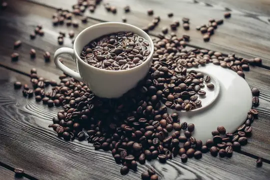Белая чашка с кофейными зёрнами на деревянном столе