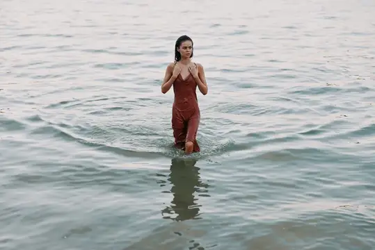 Девушка в бордовом комбинезоне стоит по колено в воде