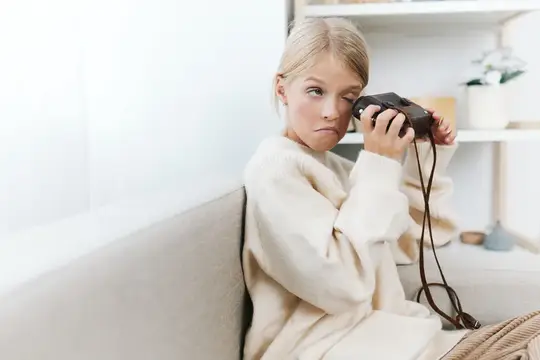 Светловолосая девочка с пленочным фотоаппаратом на диване