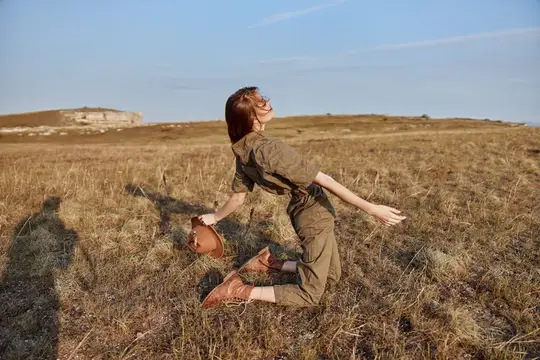 Женщина наслаждается безмятежным моментом в поле, раскинув руки и надев шляпу, чувствуя связь с природой