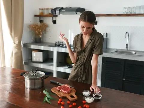 Молодая женщина готовит мясо на кухне с деревянным столом