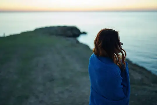 Девушка в синем пледе смотрит на море на закате