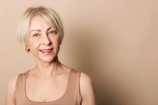 Улыбающаяся блондинка в бежевом топе на светлом фоне