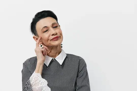Счастливая женщина старшего возраста улыбается и слушает на фоне белого фона, приложив руку к уху в жесте слушания