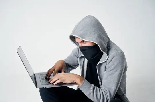 Мужчина в капюшоне и маске работает за ноутбуком