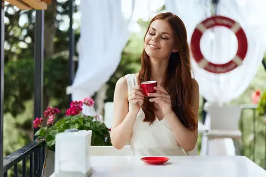 Симпатичная женщина с красной чашкой кофе на открытой террасе кафе