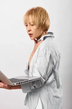 Удивлённая зрелая женщина держит ноутбук, работает с технологиями для удалённого общения