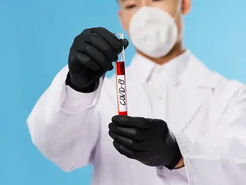 Медик в маске и перчатках держит пробирку с анализом на COVID-19