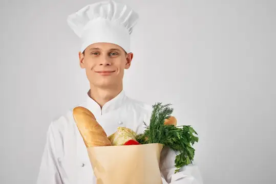 Мужчина в одежде повара держит пакет с продуктами, готовит еду на кухне