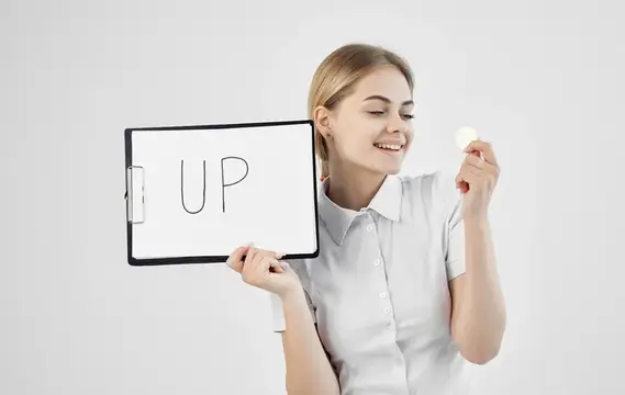 Улыбающаяся блондинка держит планшет с надписью UP и монету