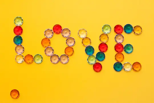 Слово LOVE выложено разноцветными стеклянными каплями на жёлтом фоне