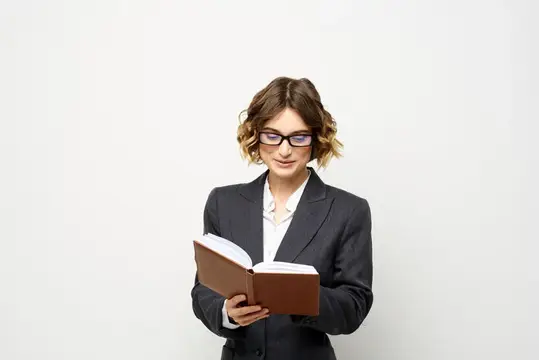 Молодая женщина в очках и деловом костюме читает книгу