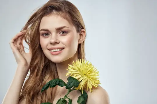 Улыбающаяся девушка с жёлтой хризантемой у лица на сером фоне