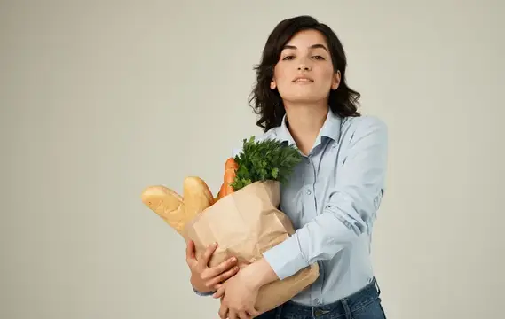 Молодая женщина с бумажным пакетом продуктов на светлом фоне