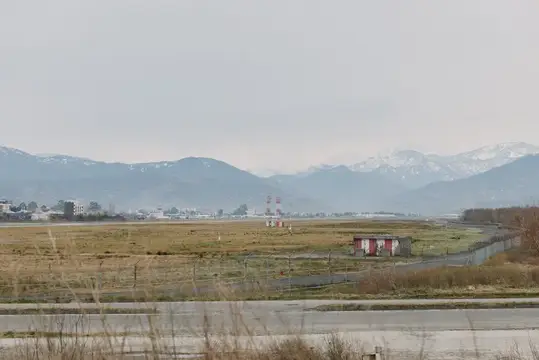 Пустынное поле с постройками на фоне заснеженных гор в пасмурный день