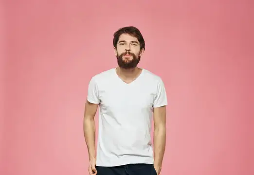 Бородатый мужчина в белой футболке на розовом фоне