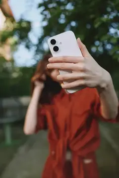Девушка в красном платье делает селфи на смартфон в парке