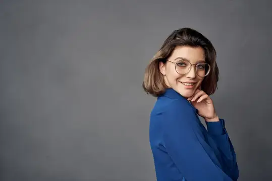 Улыбчивая шатенка в очках и синей рубашке на сером фоне