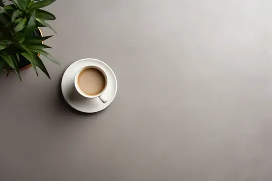 Чашка кофе с молоком на сером столе рядом с зелёным растением