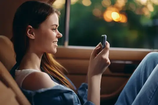 Улыбающаяся девушка смотрит в телефон в салоне автомобиля