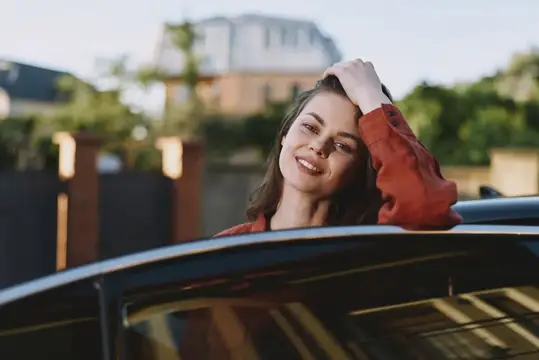 Улыбающаяся темноволосая женщина выглядывает из люка автомобиля на закате