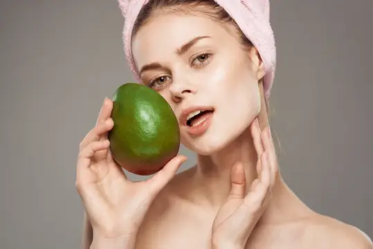На фотографии высокого качества изображена жизнерадостная женщина с обнаженными плечами, держащая манго