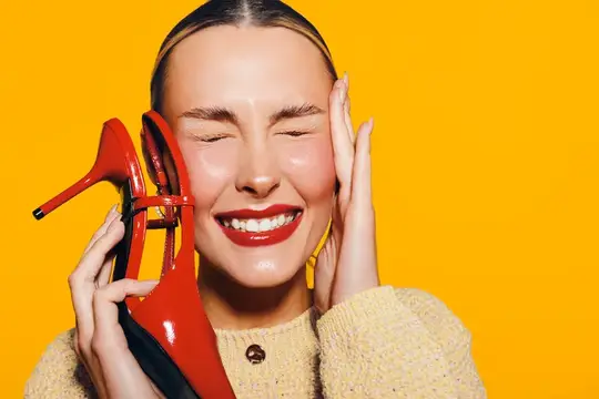 Улыбающаяся девушка с красными туфлями на жёлтом фоне