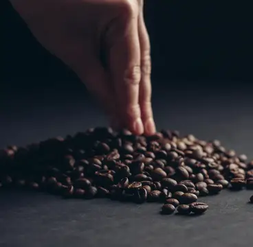 Рука касается горки кофейных зёрен на тёмном столе