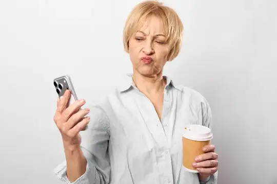 Блондинка с кофе недовольно смотрит на экран смартфона