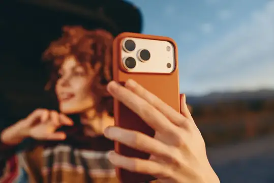 Рыжеволосая девушка фотографирует себя на смартфон в оранжевом чехле