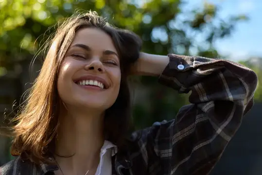 Улыбающаяся темноволосая женщина с закрытыми глазами на фоне зелени