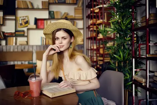 Молодая блондинка в соломенной шляпе с книгой в кафе