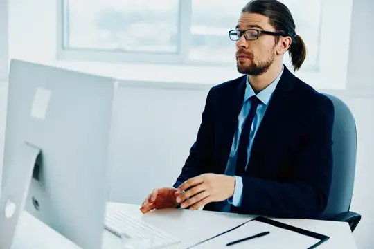 Мужчина с длинными волосами в костюме работает за компьютером в офисе