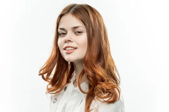 Симпатичная рыжеволосая женщина улыбается, демонстрируя косметику на лице крупным планом на светлом фоне
