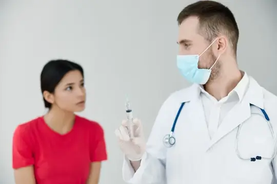 Пациент в больнице смотрит на врача, у которого в руке шприц для инъекции