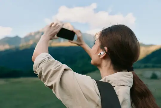 Девушка в наушниках фотографирует горы на смартфон