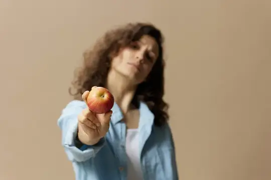 Кудрявая девушка протягивает спелое яблоко на бежевом фоне