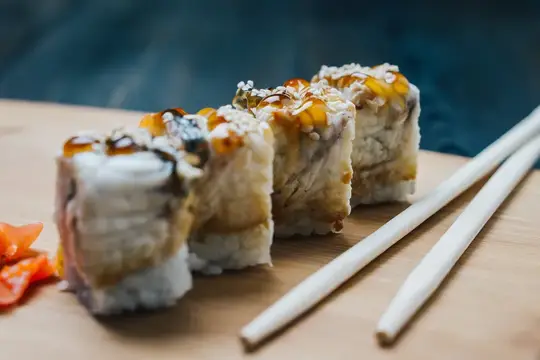 Аппетитные роллы с соусом и палочками на деревянной доске