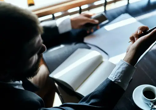 Бородатый мужчина в костюме делает записи за столом в кафе