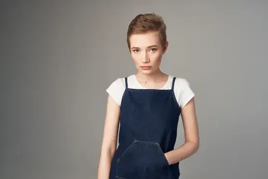 Молодая женщина с короткой стрижкой в джинсовом сарафане на сером фоне