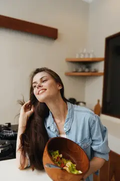 Улыбающаяся темноволосая женщина с салатом на кухне