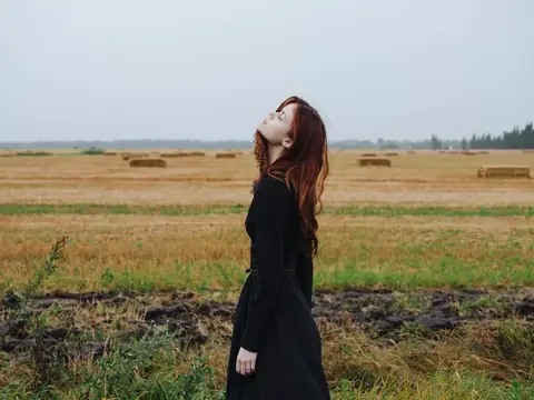 Красивая женщина в чёрном платье идёт по полю на природе осенью