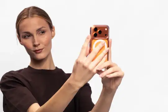 Светловолосая девушка делает селфи на смартфон в оранжевом чехле
