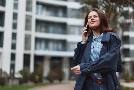 Улыбающаяся темноволосая женщина говорит по телефону на улице