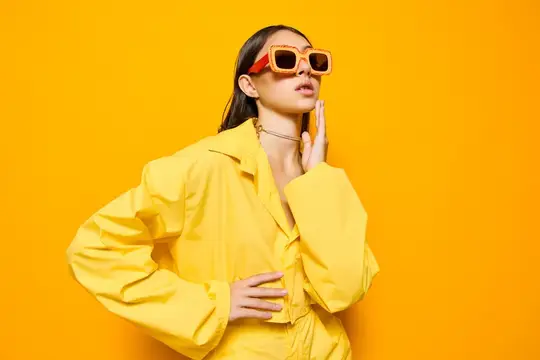 Молодая женщина в желтом костюме и солнцезащитных очках на оранжевом фоне