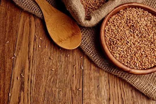Деревянная ложка и глиняная миска с пшеницей на мешковине