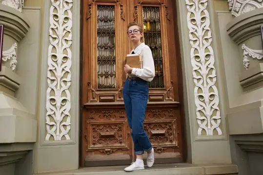 Девушка в очках с книгой стоит у резных деревянных дверей