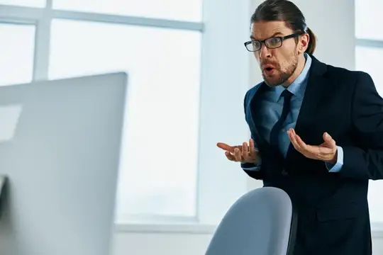 Удивлённый мужчина в очках и костюме у монитора в офисе